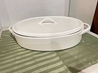 Top view of white oval lidded casserole on cloth showing overall form, handles, and lid detail