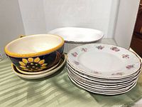 Group shot of sunflower bowls with saucers, stack of floral plates, white oval baking dish