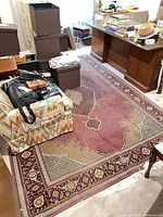Full view of oriental area rug with burgundy field, floral borders, fringe, partially covered by furniture