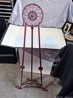 Full view of plum metal easel with scrollwork top and curved feet