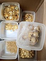 Overview of box with several tubs of gold-tone beads, charms and findings