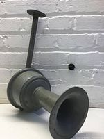 Full view of grey metal siren showing horn, housing, mounting rod