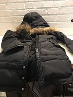 Front view of black Pajar parka with fur-trim hood laid flat