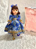 Front view of Madame Alexander Hanukkah doll on stand with menorah and partial view of box