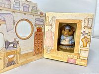 Figurine seated inside opened display box showing sewing-room graphics