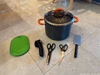 All seven items composed together on floor: stockpot with lid, grater, can opener, two scissors, green pot holder