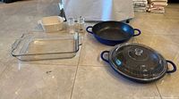 All cookware laid out: glass baking dish, ceramic dish, two grinders, two blue pans with lid
