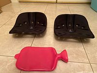 Two black BackJoy Core supports and red hot water bottle on tile floor