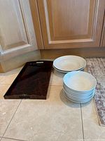 Stack of eight small bowls, two larger bowls, and dark brown rectangular tray grouped on tiled floor