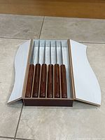 open wooden box showing six knives in individual slots