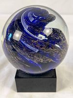 Front view of glass paperweight on base showing blue swirl and gold flecks