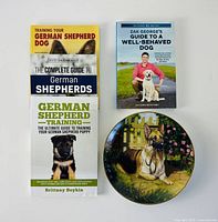 Three German Shepherd training books, Zak George training book and decorative plate overview