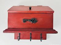 Front view of red wooden key box showing decorative key and three hooks