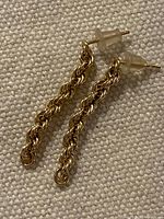 Both rope-chain gold earrings with backs visible on fabric background