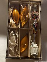 Box with three amber ornaments and tree topper showing colours and shapes