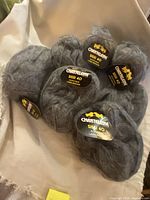 Front view of seven grey yarn skeins with Chanteleine Sissi 40 labels visible