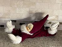 Full view of velvet elf doll lying on countertop showing suit, hat, boots.