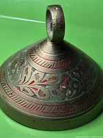 Side view of brass bell showing loop hanger and etched, colored floral designs