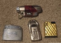 Group shot of all four lighters: Iroda torch, brushed metal flip-top, silver car-shaped, gold-tone patterned