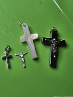 All four pieces laid out: black hematite cross with corpus, white stone cross, detached corpus, small silver cross pendant