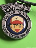 Close-up of pendant front showing text and Ash graphic