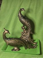 Both peacock statues on green tray showing relative sizes