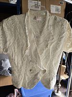 Full view of cream lace blouse on hanger showing front, buttons, collar