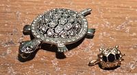Large and small turtle brooches together on surface