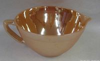 Side view of peach lustre Fire-King mixing bowl showing handle, spout and exterior finish