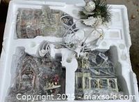 Styrofoam tray holding three wrapped ceramic houses, figurine, and bundled light cords