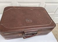 Closed brown vinyl suitcase top view showing handle and exterior wear