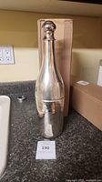 Opened metal champagne bottle-shaped cooler showing full form next to box