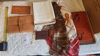 Full lot showing leather folio, wallet, white pillowcases, brown and white/orange scarves, orange placemats/napkins set, woven pouch