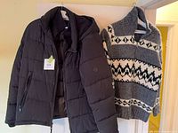 Front view of both garments hanging: black puffer jacket and grey patterned sweater