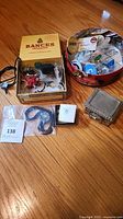 Lot overview showing tin of pins, cigar box, bolo tie in bag, trinket box and pin box