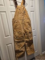 Full view of tan Carhartt canvas bib overalls hanging