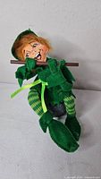 Front view of Annalee leprechaun doll seated on stone, flute in hands