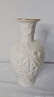Full front view of ivory porcelain vase showing embossed floral design and gold rim