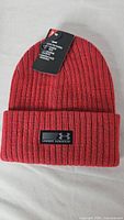 Front view of red Under Armour ribbed knit beanie with tags attached