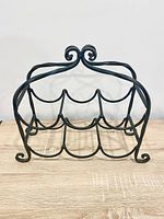 Front view of black wrought iron wine rack showing six bottle slots and scrollwork top