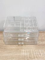 Front view of stacked clear acrylic organizer showing top compartments and three drawers