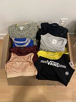 Open box showing stacked tops including Vans, sequined top, sports bra, knit top