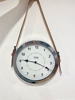 Front view of Home Collection wall clock hanging by strap