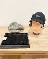 All three items displayed: Levi’s trapper hat on mannequin, grey flat cap, folded Calvin Klein scarf with tags