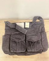 Full view of grey corduroy bag with flap pockets and strap