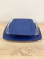 Stacked view of both glass baking dishes with blue lids showing size difference and handles