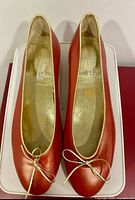 Top view of both red leather ballet flats showing gold trim and bow, interior branding visible