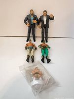 Group shot of two suited figures standing, two masked wrestlers lying, sealed stamp in foreground