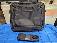 Front view of black Dell laptop case on blue surface, shows exterior pocket and Dell logo