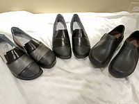 All three pairs of Naot slip-on shoes displayed side-by-side on bed
